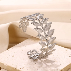 Macro shot of silver olive leaf open bangle with intricate texture on marble base