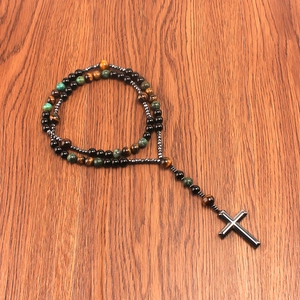 Detailed view of tiger eye beads and black cross pendant on a textured wood surface