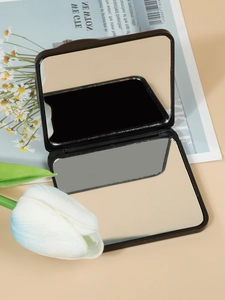 Close-up of a mini black square folding makeup mirror on a stylish magazine background