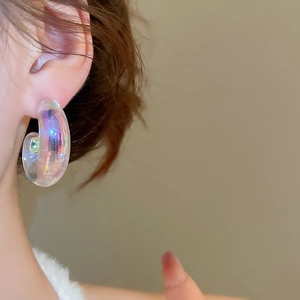 Close-up of rainbow iridescent C-shape acrylic earring worn on ear with light refraction
