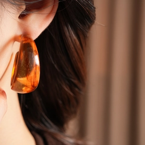 Close-up of amber resin C-shaped earring on model with vintage aesthetic detail