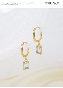 Detail of gold titanium earrings with light blue square zircon pendant on white fabric