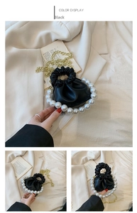 Close-up of black pleated mini bucket bag featuring white pearl handle and gold chain strap