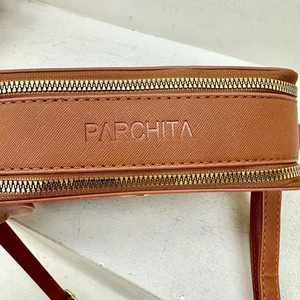 Close-up of brown textured leather bag with gold zipper detail and Parchita logo