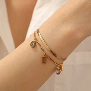 Close-up of layered gold bracelet with colorful zircon charms on a female wrist