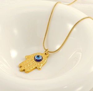 Macro shot of gold Hamsa Hand pendant with blue Evil Eye on a sleek snake chain
