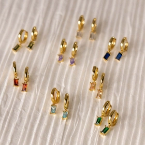 Elegant gold earrings with colorful rectangular zircon gemstones on white fabric