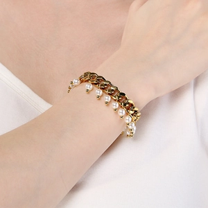 Close-up of golden Cuban chain bracelet with small white pearls on model's wrist