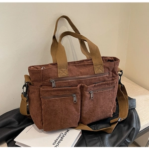 Detail of a brown corduroy tote bag with multiple zip pockets on a black bench