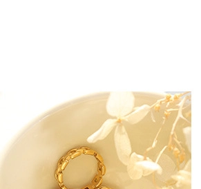 Macro shot of a golden vintage oval rose pendant on a chain inside a ceramic bowl
