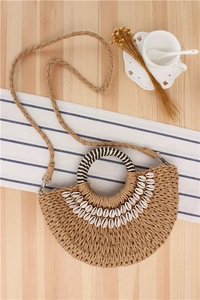 Detail of semi-circle straw woven bag with shell accents and striped handles on a table
