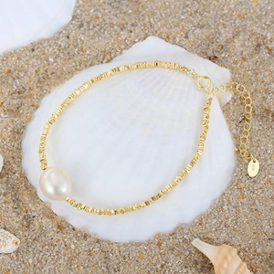 Macro view of a 925 silver bracelet with golden beads and a baroque pearl on sand