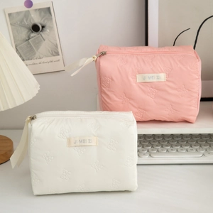 Detail of pink and white bow-quilted makeup bags with soft ribbon zippers and fabric labels