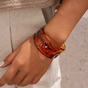 Detail showing amber resin cuff bracelet with wavy texture and translucent finish