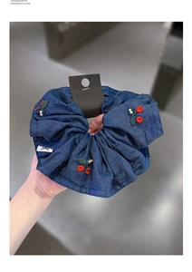 Detail of blue denim scrunchie featuring red cherry embroidery and white pearls