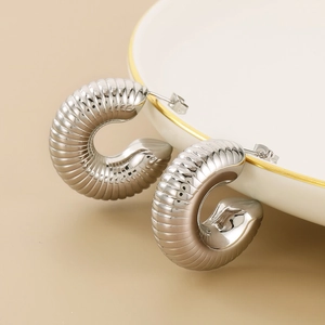 Macro shot of silver C-shape earrings with a textured spiral conch design and polished finish