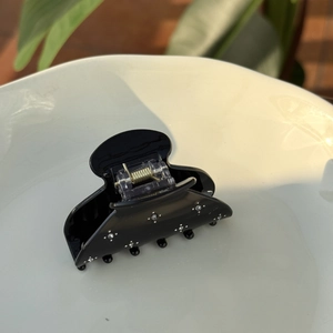 Close-up of black acetate hair claw clip with sparkling rhinestones on a white plate