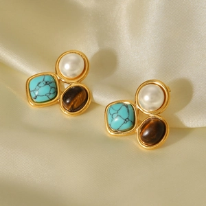 Detail of gold earrings set with pearl, turquoise, and tiger eye stone on silk fabric