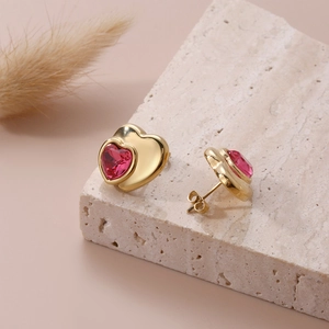 Golden heart earrings with vibrant red heart-shaped crystals on stone background