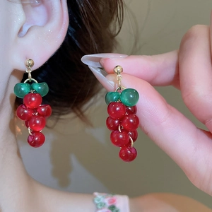 Detail shot of red resin grape tassel earrings with gold posts on a soft warm background
