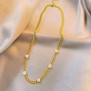 Gold Cuban chain necklace with five sparkling heart pendants on champagne satin background
