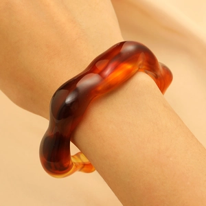 Close-up of a wide amber resin bangle with wavy edges on a woman's wrist
