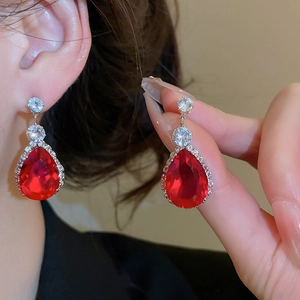 Close-up of red teardrop zircon earrings with silver settings worn by a model