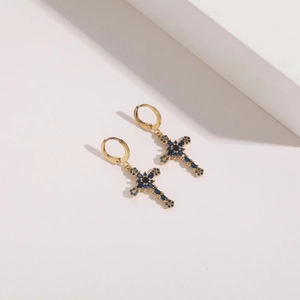 Macro detail of gold cross earrings with blue zircon stones on a white studio background