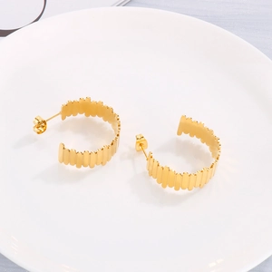 Détail macro de boucles d'oreilles créoles dorées en C avec motif texturé sur plateau blanc