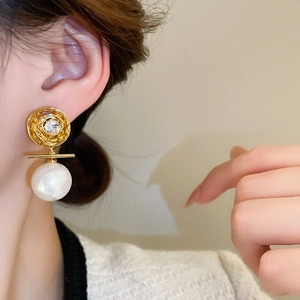 Détail de boucles d'oreilles dorées avec perle blanche et zircon portées par un mannequin