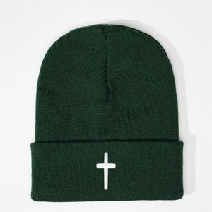 Close-up of cross embroidery on dark green knitted beanie with detailed ribbed texture
