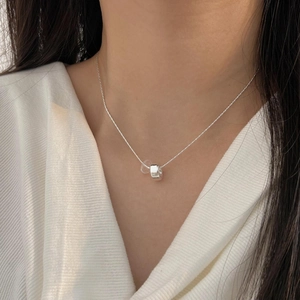 Close-up of a minimalist silver circle necklace worn by a model with a white shirt