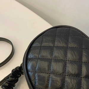 Close-up detail showing the black quilted texture and stitching of a round handbag
