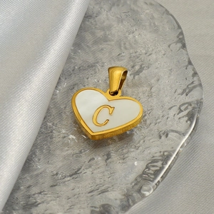 Macro shot of gold heart pendant with white pearl inlay and engraved letter C detail