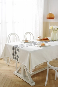 Detailed close-up of beige linen tablecloth with grey palm embroidery and white tassels