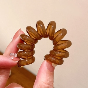 Détail macro d'un élastique spirale marron tenu à la main pour queue de cheval