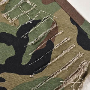 Dettaglio macro del tessuto in twill di cotone mimetico con fori consumati e frange