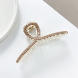 Close-up of beige acrylic hair claw clip showing cross twist design and clear teeth