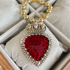 Macro detail of red enamel heart pendant with crown crest and metallic beaded chain