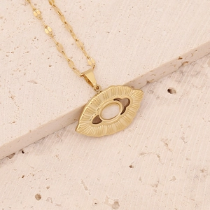 Detail of gold owl eye pendant with white gemstone on beige textured stone base