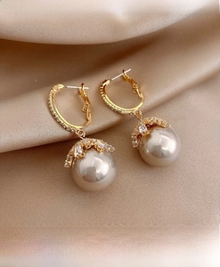 Macro shot of elegant gold pearl drop earrings with sparkling zircon accents on silk