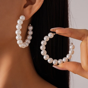 Detail view of elegant C-shaped faux pearl beaded hoop earrings on a model's ear