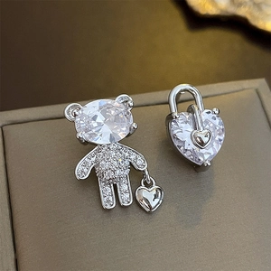 Detailed macro view of asymmetric silver teddy bear and heart lock earrings with zircons