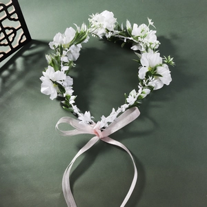 Detail of white fabric floral headband with pink ribbon on dark green background