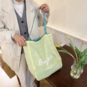 Detail of green plaid canvas tote bag with Bonjour magic print in cozy indoor setting