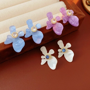 Détail de trois boucles d'oreilles fleurs en résine violette, bleue et blanche avec zircon