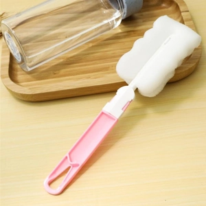 Pink long handle cup cleaning brush with wavy sponge head on a wooden tray