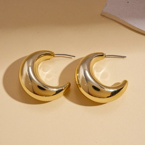 Detailed view of gold C-shaped geometric stud earrings on a minimalist stone display