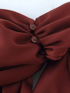 Close-up of reddish brown satin dress featuring pleated texture and button details