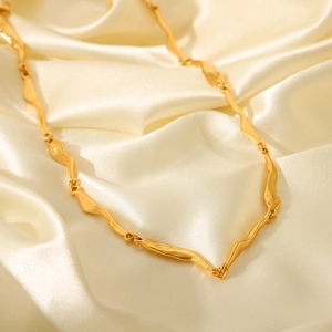 Macro shot of gold wavy link necklace on cream silk fabric with warm natural lighting